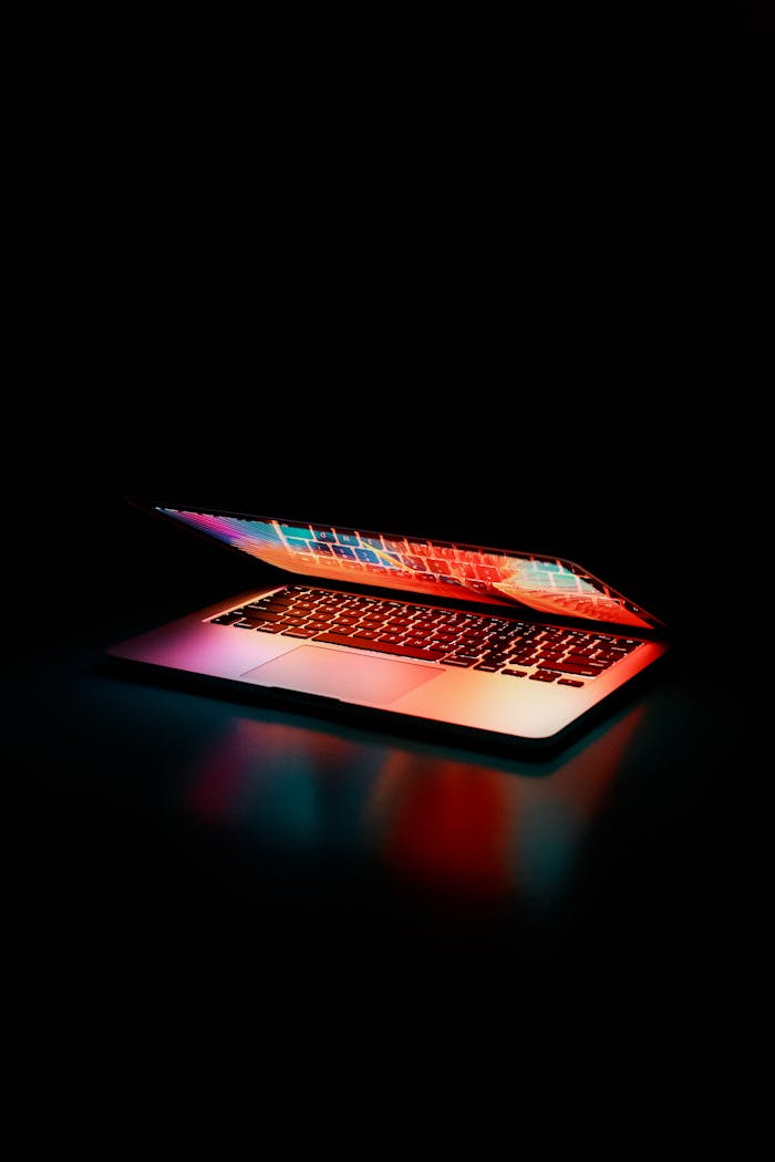 digital Laptop partially opened, emitting vibrant multicolored lights in dark setting.